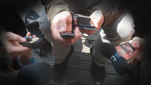 The centre of a journalism scrum. The photo is of many hands holding various kinds of recording devices around the photo taker.