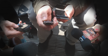 The centre of a journalism scrum. The photo is of many hands holding various kinds of recording devices around the photo taker.